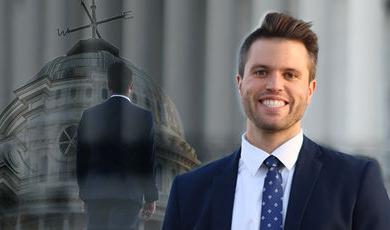 Kyle Bueno stands with a smile in the background is blurred image of him looking up at Boyden Hall 